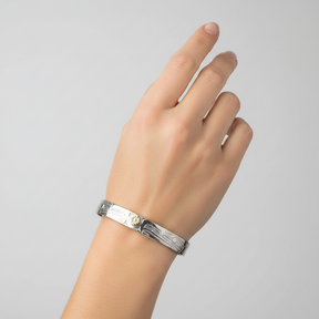 A 7mm silver-toned cuff bracelet with engraved carvings and a central gold-toned sunburst medallion, shown on a plain white background.