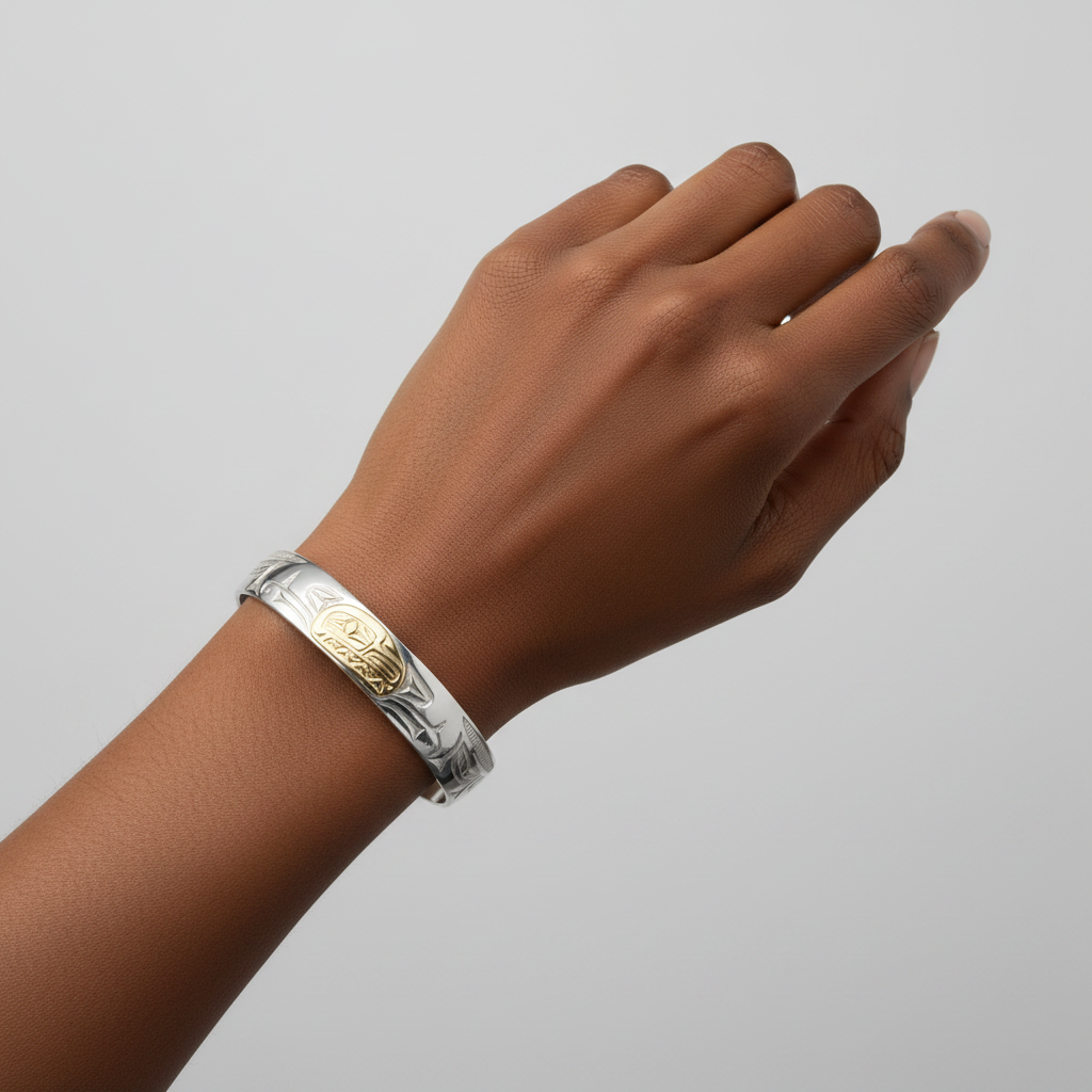A 10mm width silver cuff bracelet with engraved patterns and a central gold oval inlay featuring a carved figure, shown on a white background.