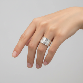 A wide sterling silver band ring featuring hand-carved, raised abstract organic patterns resembling a bird head and flowing lines, shown on a clean white background.
