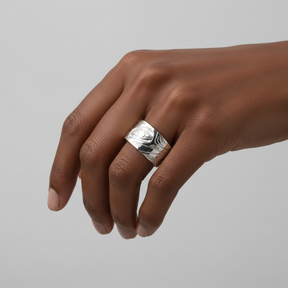 A wide silver band ring featuring hand-carved, abstract tribal-style patterns, shown on a clean white background.